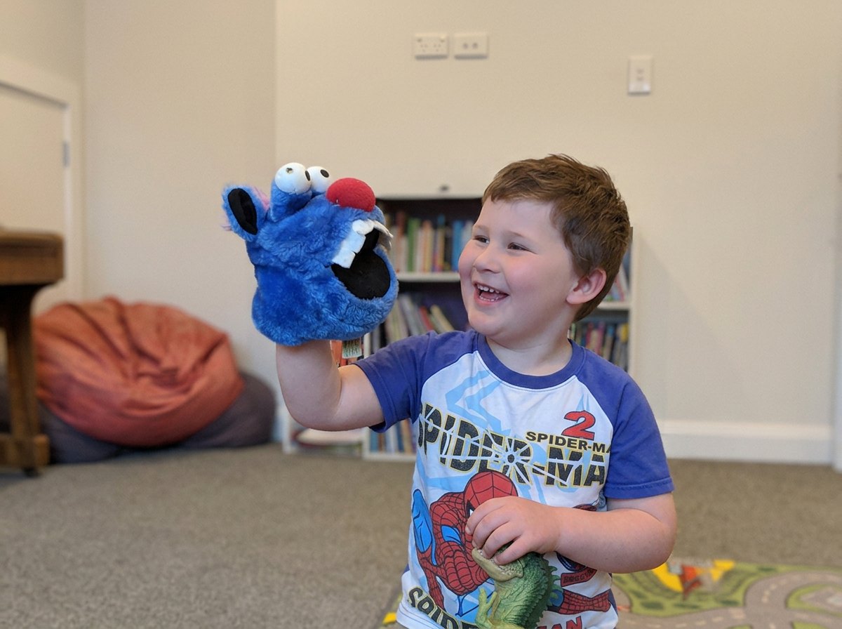 A young boy laughing while playing with a puppet