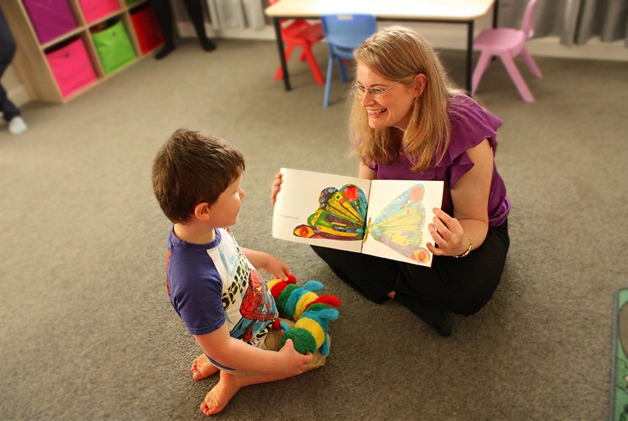 Sarah and a young boy sitting on the floor sharing a picture book