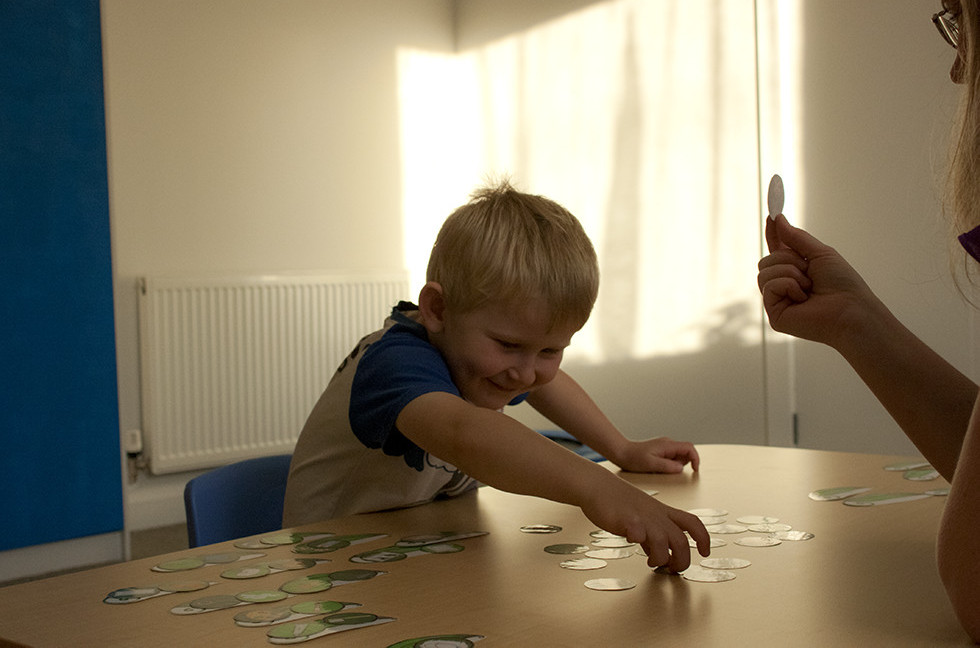 A young boy reaching across a table of picture cards during a speech therapy session