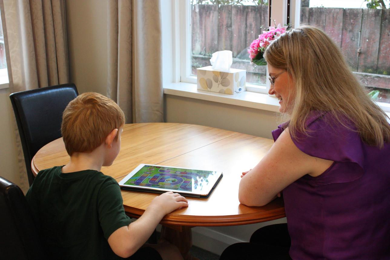 Sarah and a young boy sitting at a table together, playing a language game on a tablet